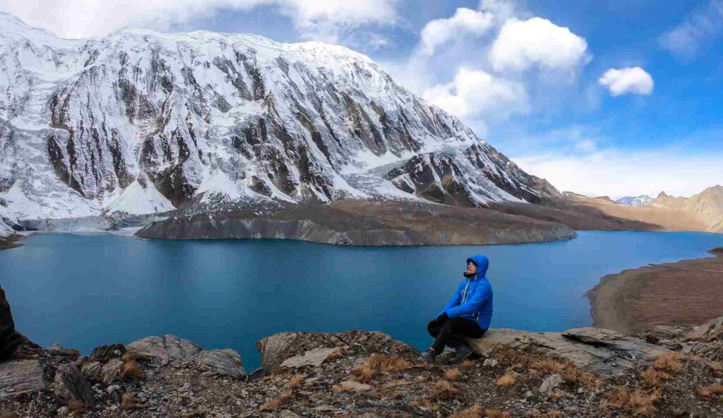 A man sitting the turquoise colored Tilicho lake in Himalayas